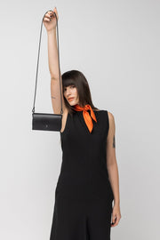 Femme en robe noire tenant petit sac en cuir PYKOK Kora par une anse
