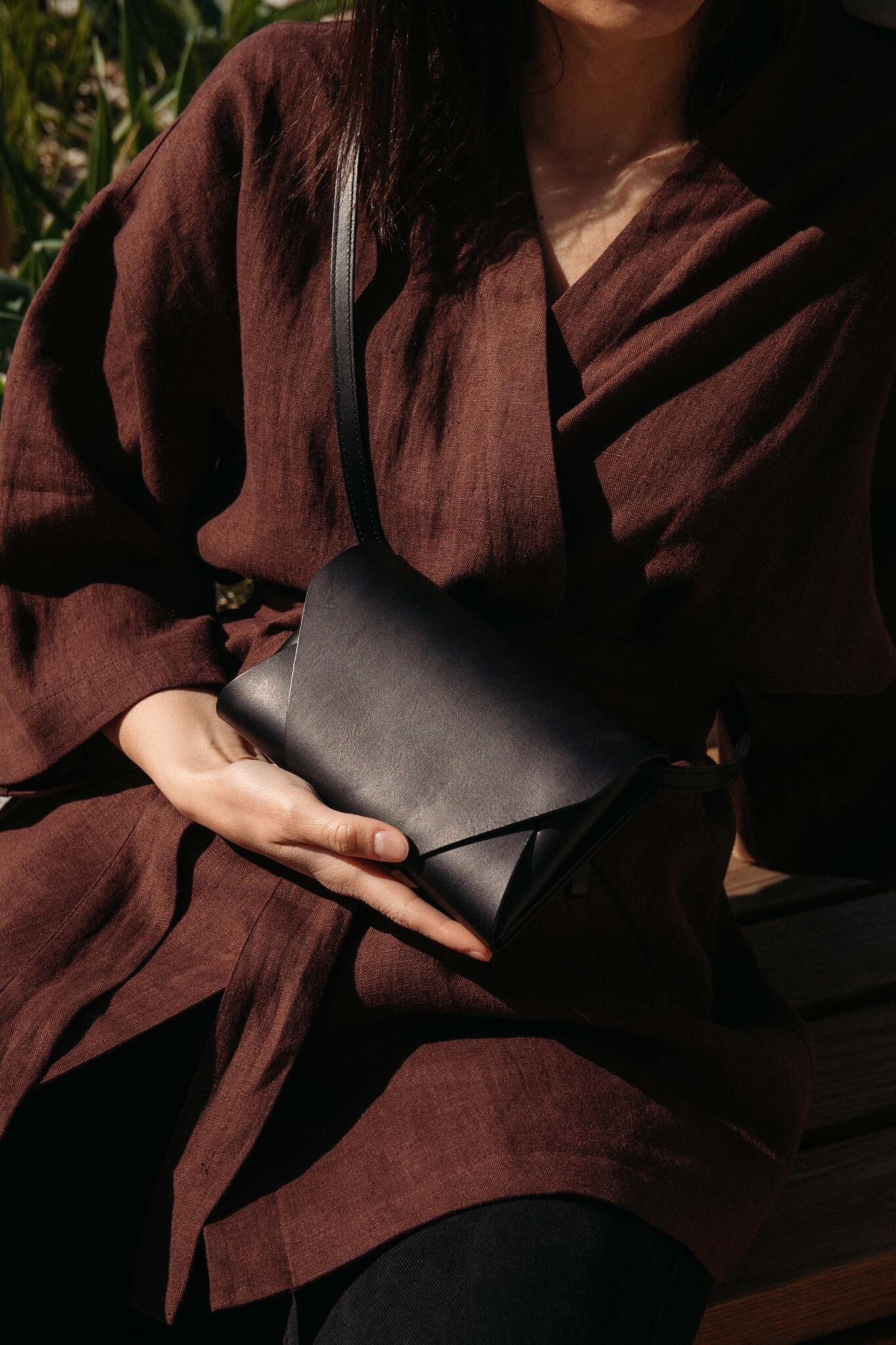 Pochette-portefeuille en cuir noir Stella Soomlais tenue sur les genoux, portée en bandoulière, lumière naturelle
