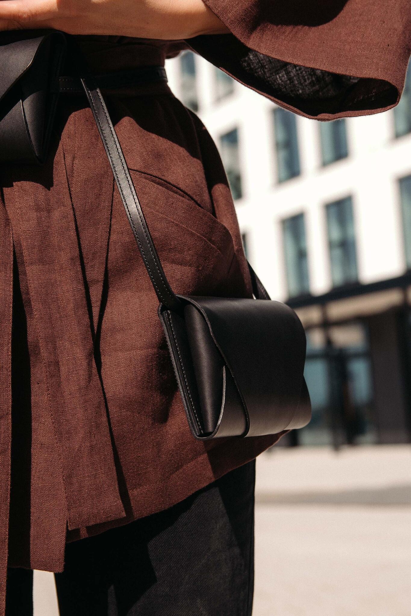Pochette-portefeuille en cuir noir Stella Soomlais portée à la hanche en bandoulière, vue de profil en ville