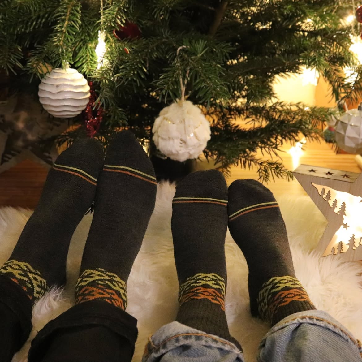 Deux paires de chaussettes en laine mérinos foncées à motifs portées ensemble près d'un sapin de Noël, Baltland