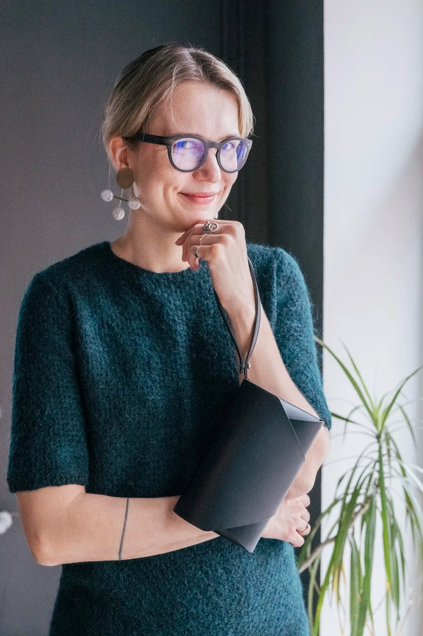 Pochette bandoulière en cuir noir Stella Soomlais tenue repliée sous le bras avec dragonne au poignet