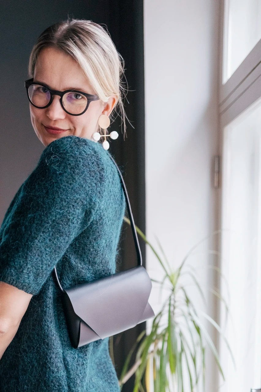 Pochette bandoulière en cuir noir Stella Soomlais portée à l'épaule, vue de profil