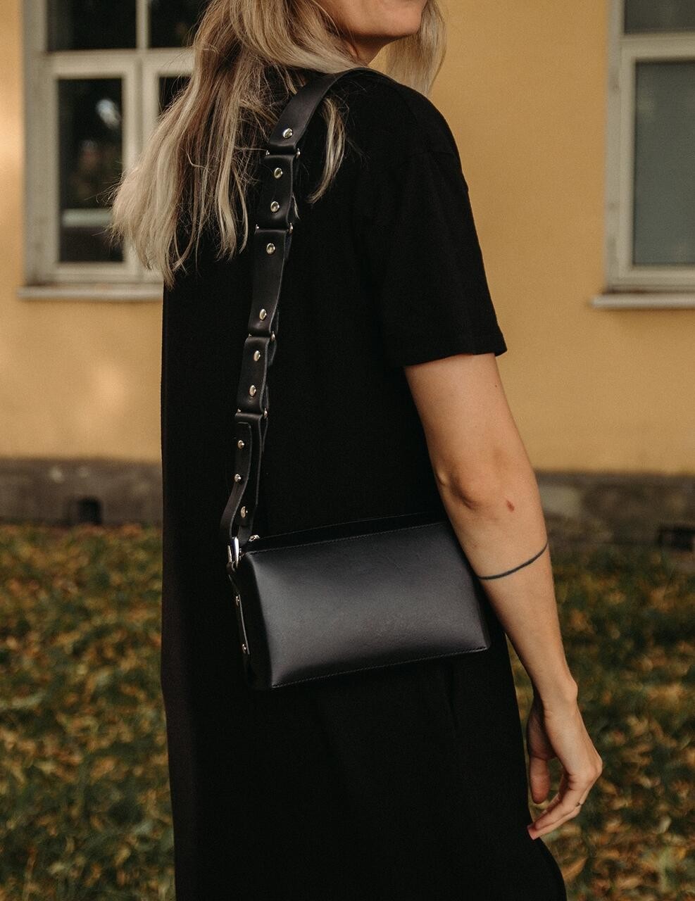 Sac bandoulière en cuir noir Stella Soomlais, porté à l'épaule avec sangle large rivetée