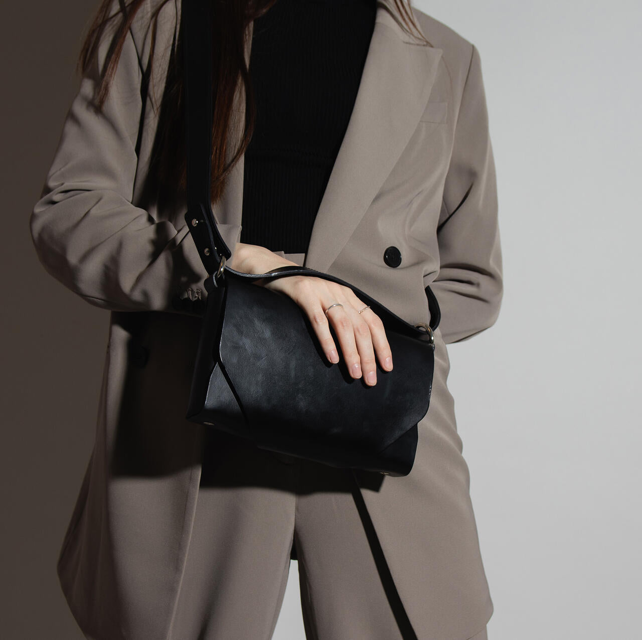 Sac bandoulière en cuir noir Stella Soomlais porté croisé, main posée sur le rabat
