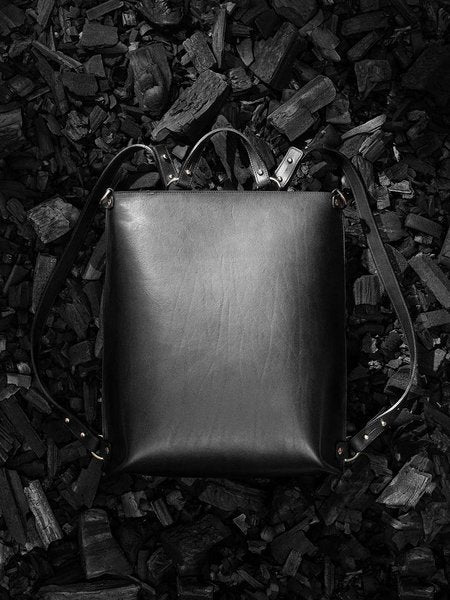 Sac à dos en cuir noir Stella Soomlais, posé à plat sur du charbon, vue de dos
