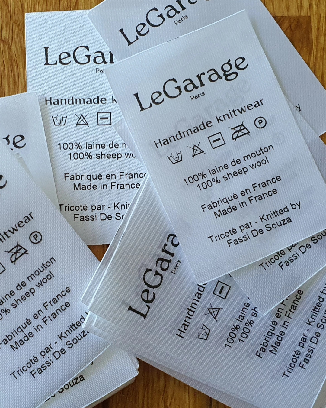 Étiquettes en papier blanc imprimées en noir, instructions de lavage et mention 100 pourcent laine, sur fond bois clair