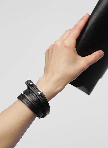 Main tenant la pochette-portefeuille en cuir noir Stella Soomlais, lanière portée en bracelet au poignet