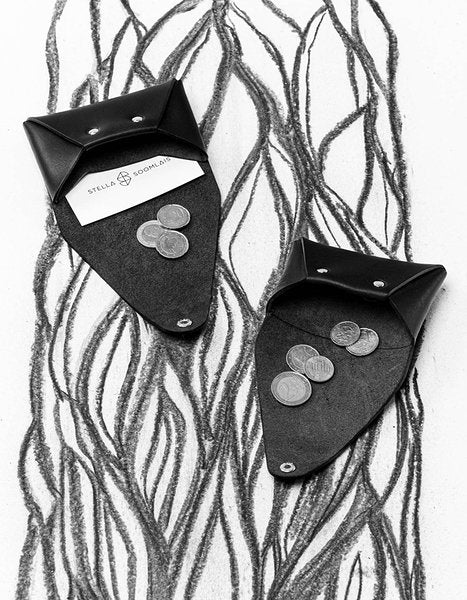 Deux porte-monnaie en cuir noir Stella Soomlais ouverts avec pièces et carte, fond illustré noir et blanc