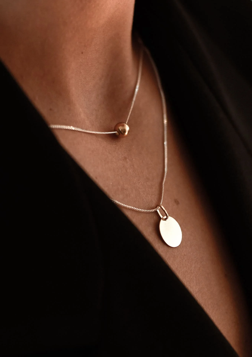 Collier Bubble NO MORE en plaqué or porté avec pendentif ovale argenté, sur top noir