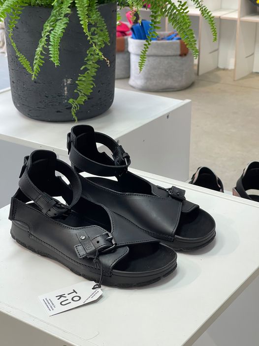 Sandales TOKU Athens en cuir noir à bride ajustable, posées sur présentoir