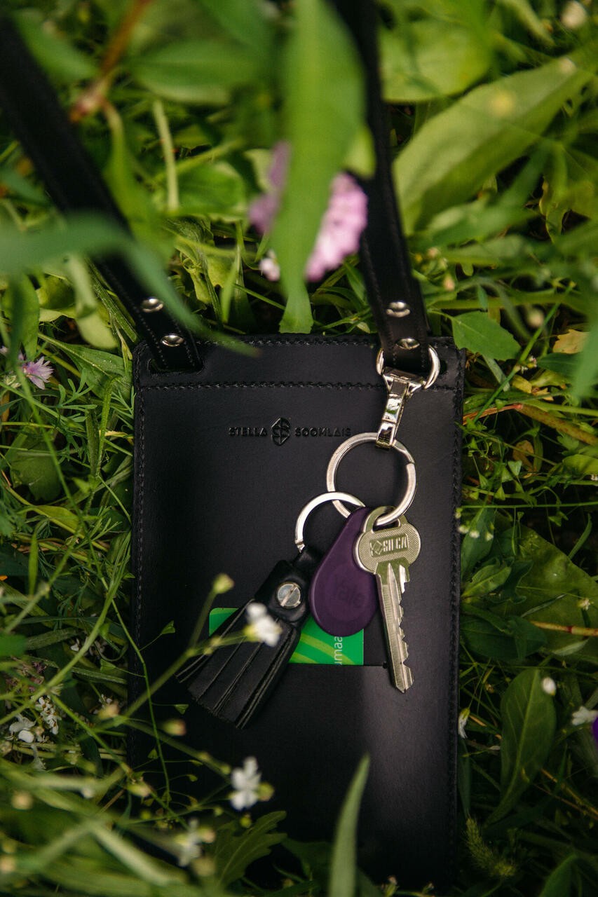 Pochette téléphone en cuir noir Stella Soomlais dans la verdure, clés fixées au mousqueton, tannage végétal