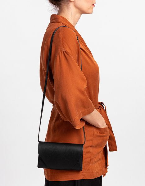 Pochette-portefeuille en cuir noir Stella Soomlais portée en bandoulière sur chemise rouille, vue de profil