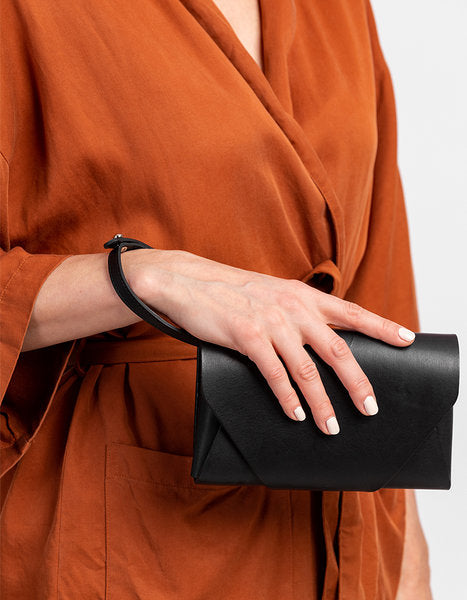 Pochette-portefeuille en cuir noir Stella Soomlais tenue à la main, lanière enroulée au poignet
