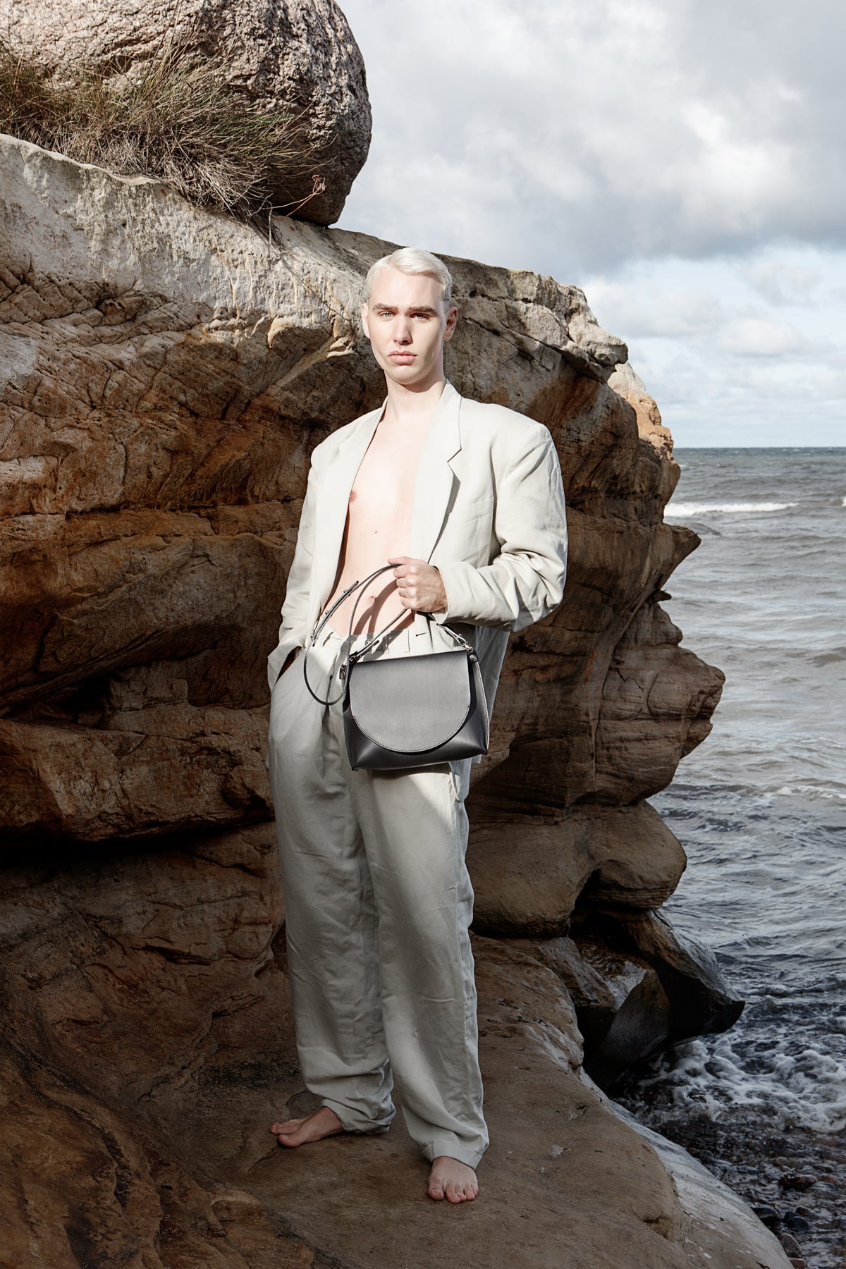Sac à main en cuir noir Stella Soomlais tenu à la main par un modèle en bord de mer