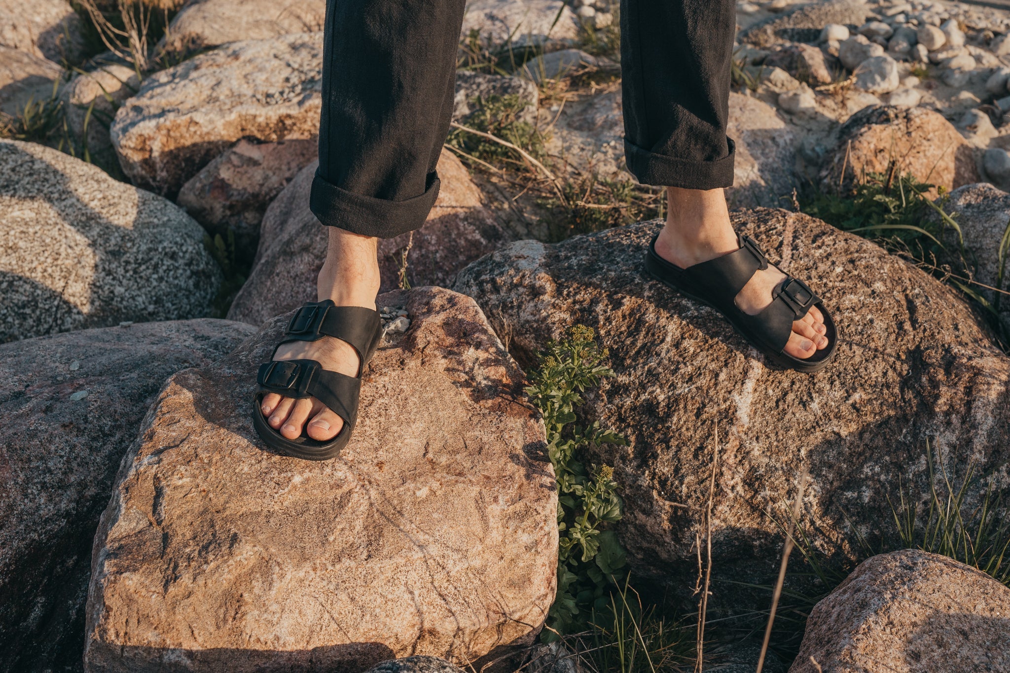 Homme portant des sandales en cuir noir Märt sur des rochers au coucher de soleil