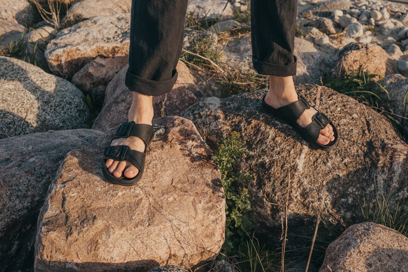 Homme portant des sandales en cuir noir Märt sur des rochers au coucher de soleil