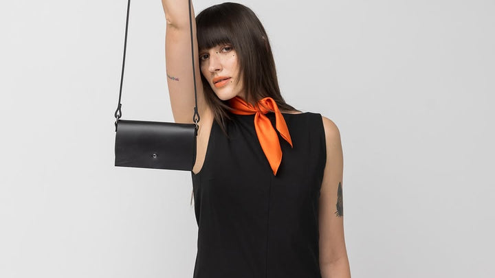 Femme en robe noire tenant petit sac en cuir PYKOK Kora par une anse