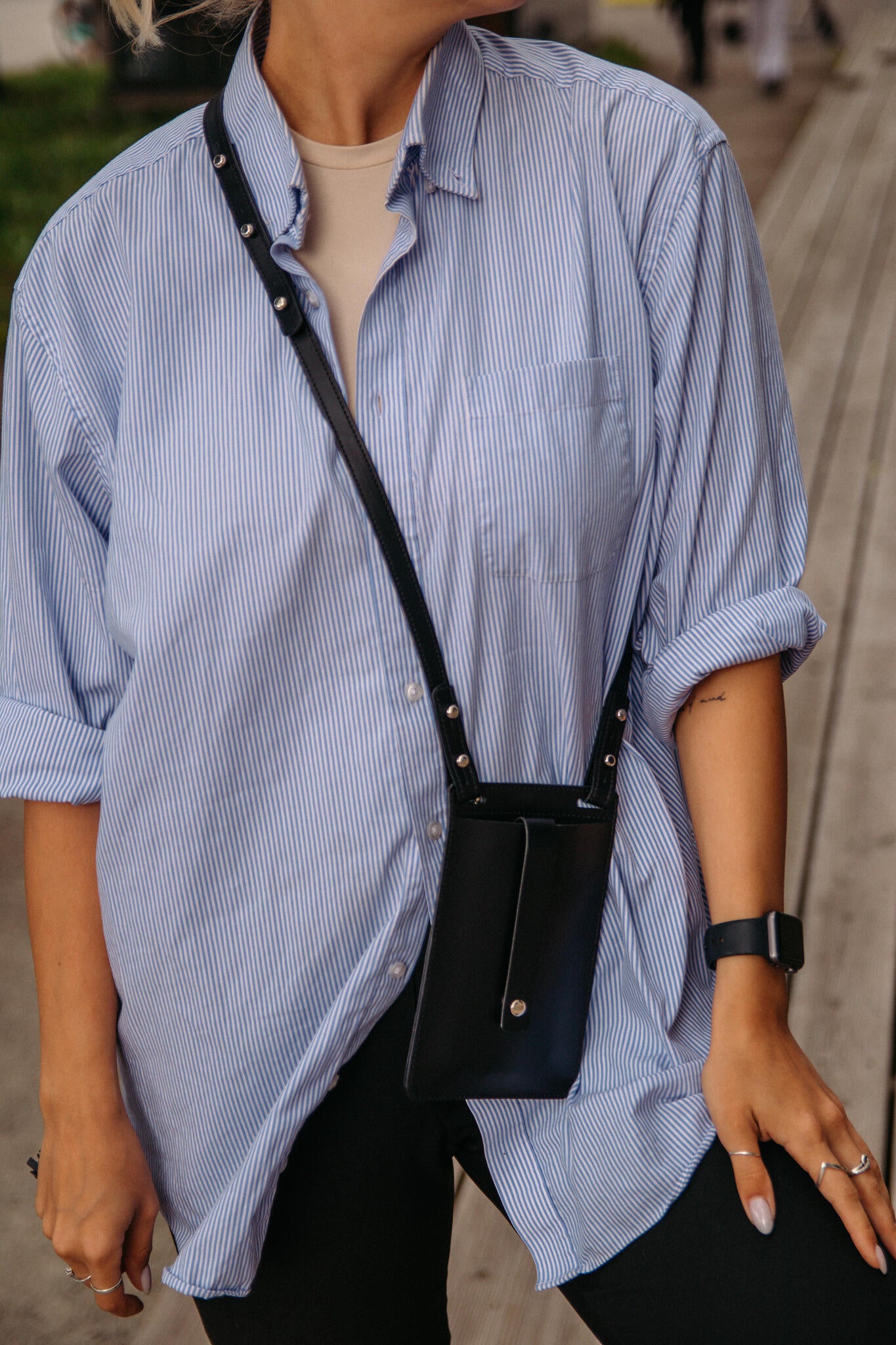 Pochette téléphone en cuir noir Stella Soomlais portée croisée sur chemise rayée, rivets nickel apparents