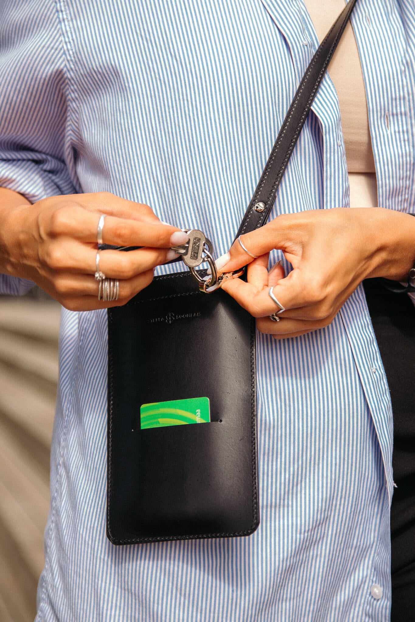 Mains fixant un trousseau de clés au mousqueton de la pochette téléphone en cuir noir Stella Soomlais