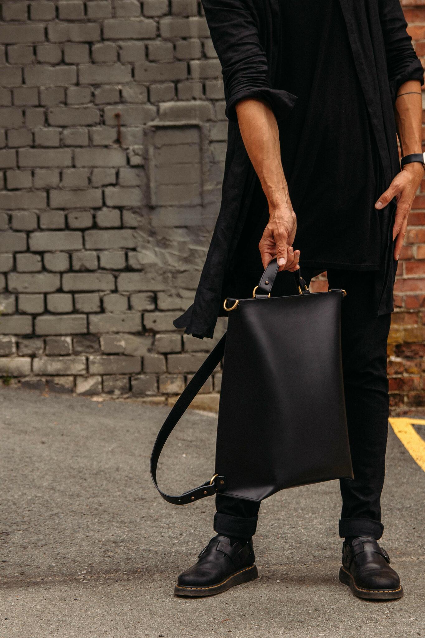 Sac à dos en cuir noir Stella Soomlais tenu en main, sangle d'épaule ajustable déployée