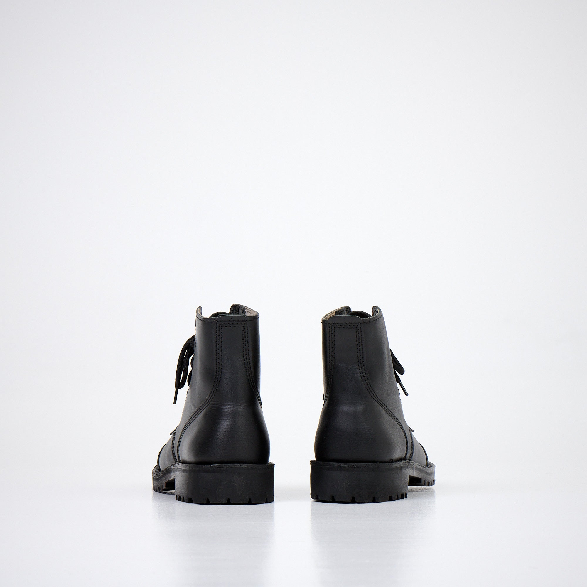 Bottines en cuir noir fait main sur parquet, ambiance intérieure épurée