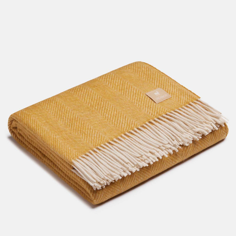 Plaid en laine d'alpaga motif chevrons ocre et blanc déplié sur fond gris