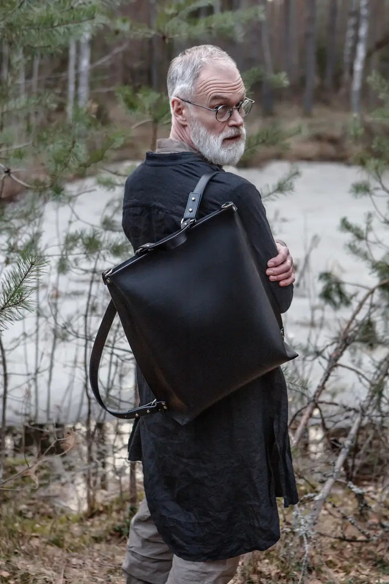 Sac à dos en cuir noir Stella Soomlais porté à l'épaule par un modèle homme en forêt
