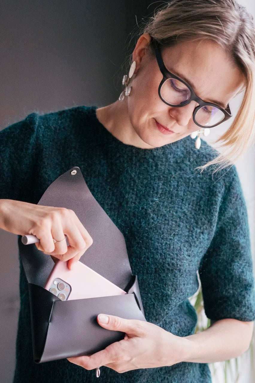 Pochette bandoulière en cuir noir Stella Soomlais ouverte, un smartphone glissé à l'intérieur