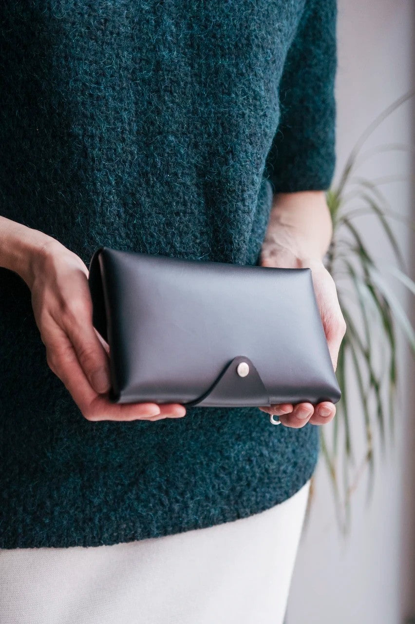 Pochette bandoulière en cuir noir Stella Soomlais tenue à deux mains, détail du bouton pression nickel