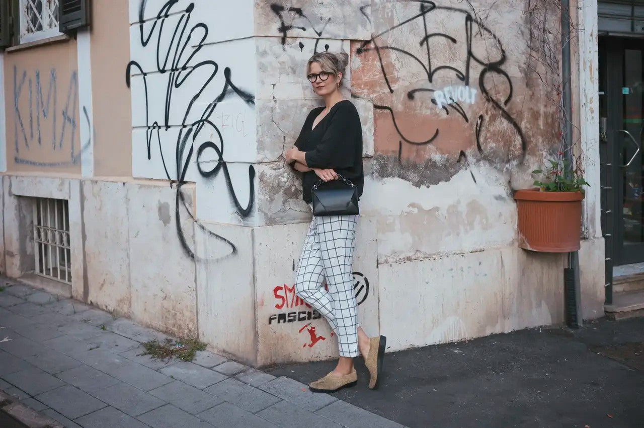 Sac à main en cuir noir Stella Soomlais fait main en Estonie, tenu par la poignée devant un mur urbain