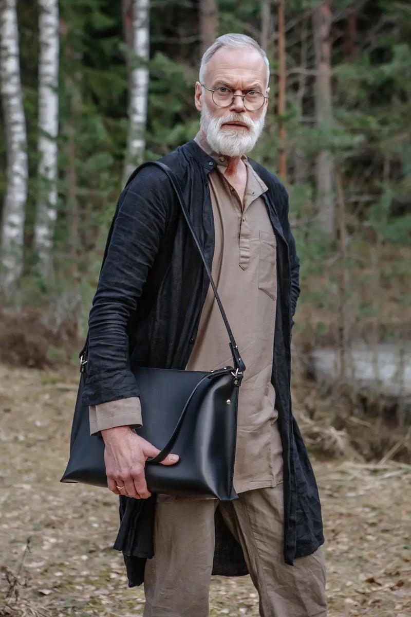 Sac à main en cuir noir Nothing to Declare Stella Soomlais, porté en bandoulière par un homme en forêt