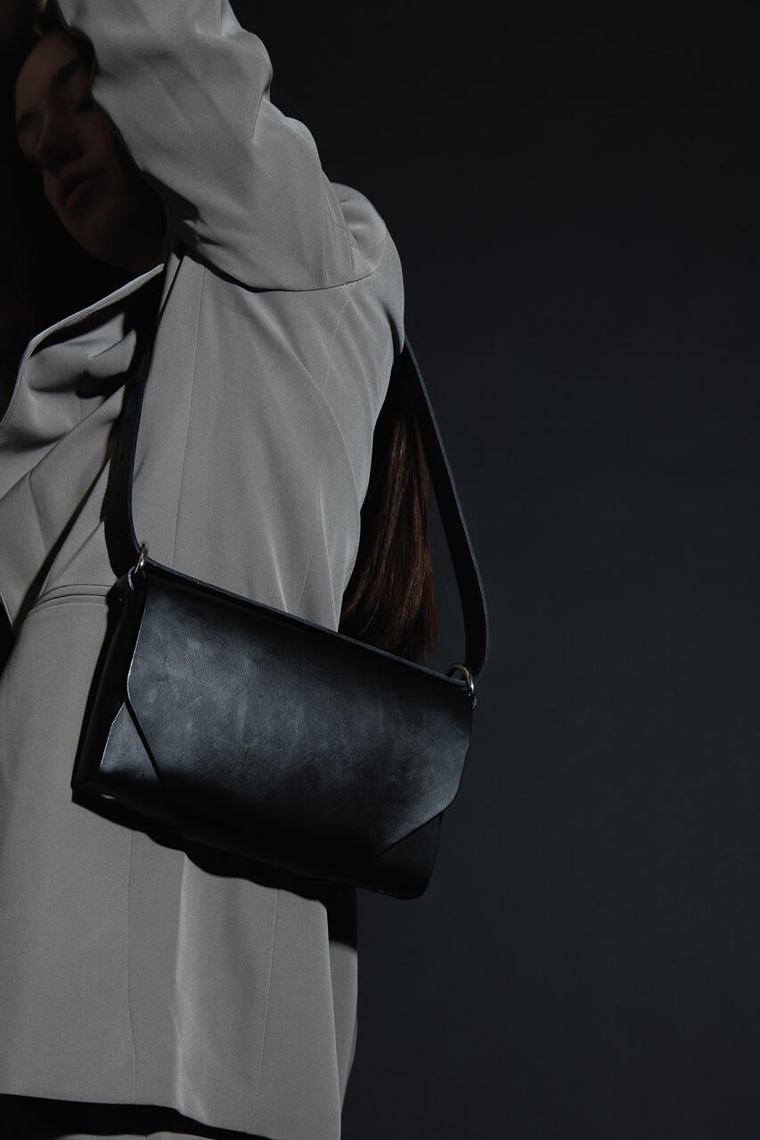 Sac bandoulière en cuir noir Stella Soomlais, vue rapprochée du rabat asymétrique porté à l'épaule