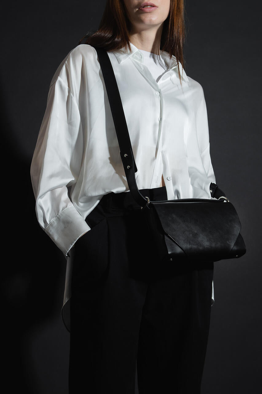 Sac bandoulière en cuir noir Stella Soomlais à tannage végétal porté croisé sur une chemise blanche