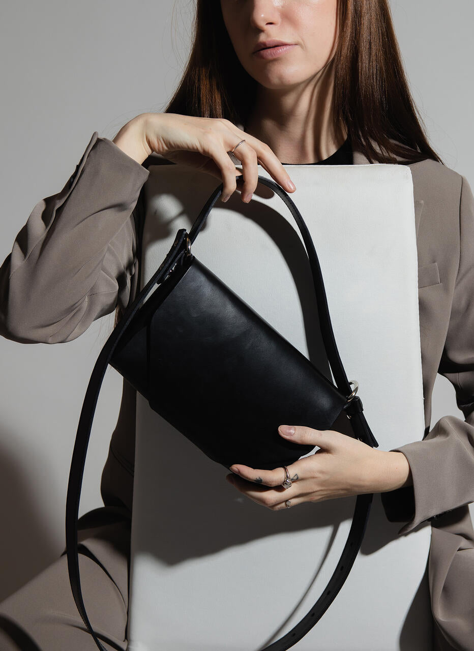 Sac bandoulière en cuir noir Stella Soomlais tenu en main, sangle ajustable et anneau nickel