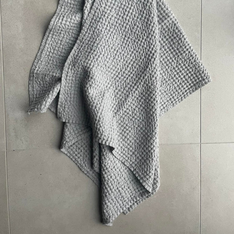 Grande serviette en lin nid d'abeille gris perle KOOS, drapée sur sol carrelé clair