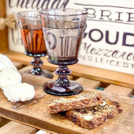 Verres à pied abeille colorés La Rochère aubergine et ambré, ambiance apéro avec fromage de chèvre et pain aux fruits secs sur planche en bois