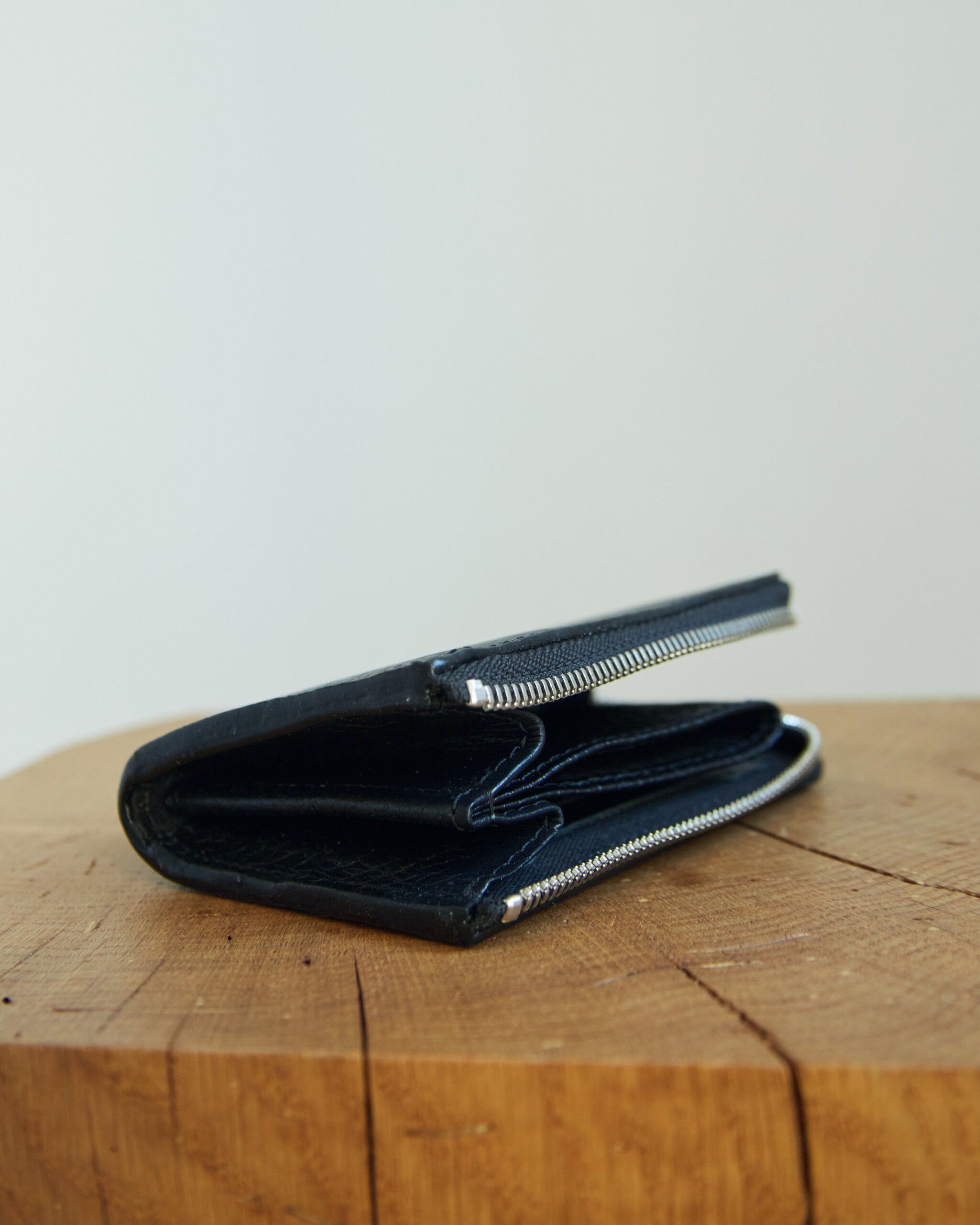 Portefeuille MACA Lava Flow en cuir noir, ouvert et zippé sur une souche de bois clair