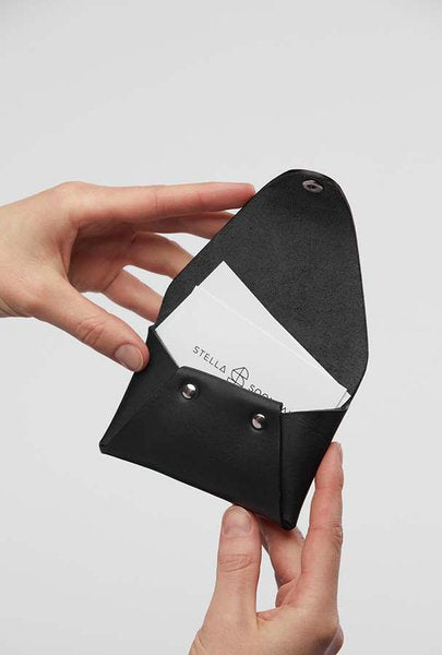Porte-monnaie en cuir noir Stella Soomlais tenu ouvert en main, carte glissée dans la poche