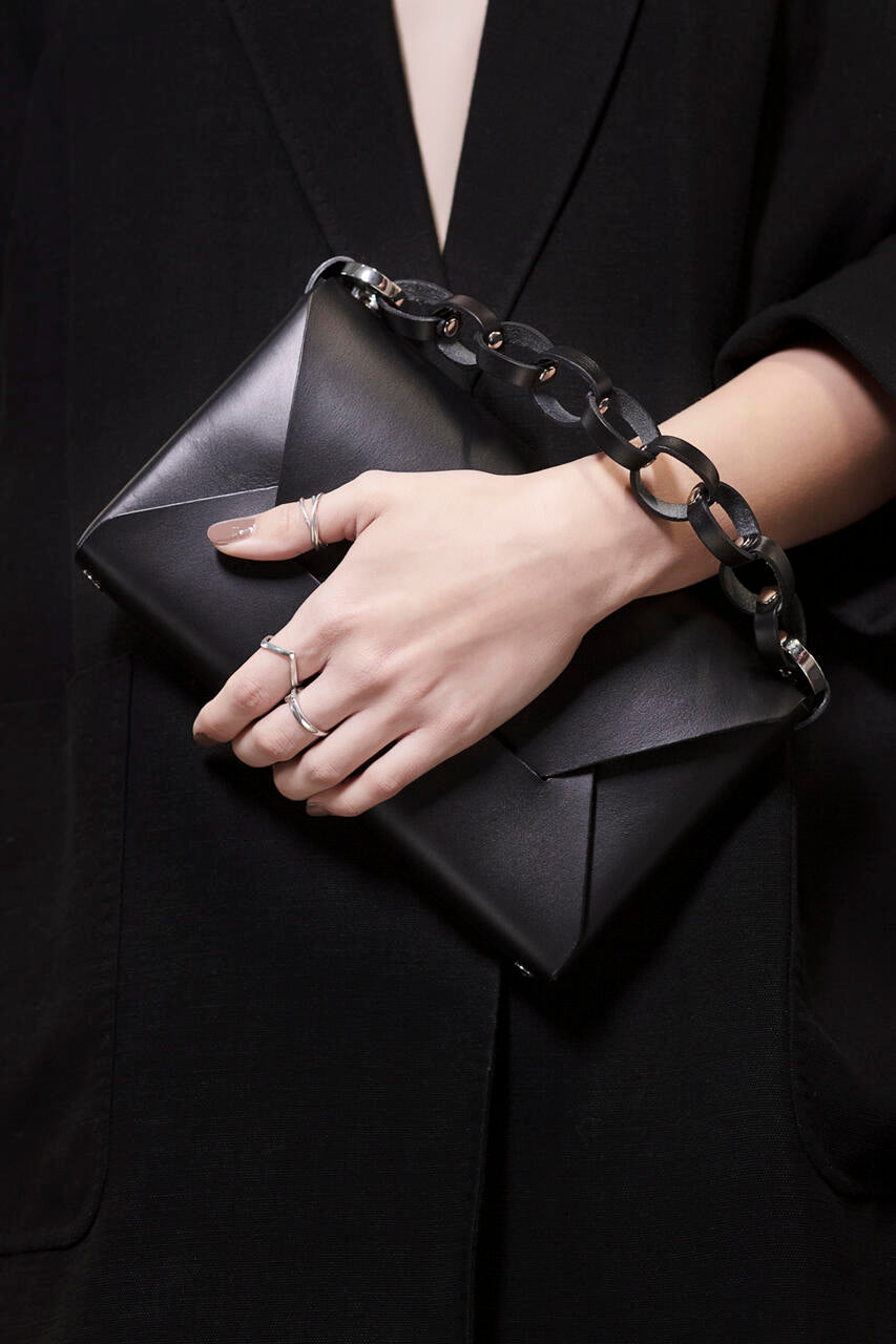 Sac à main en cuir noir Stella Soomlais tenu en pochette, chaîne à gros maillons au poignet