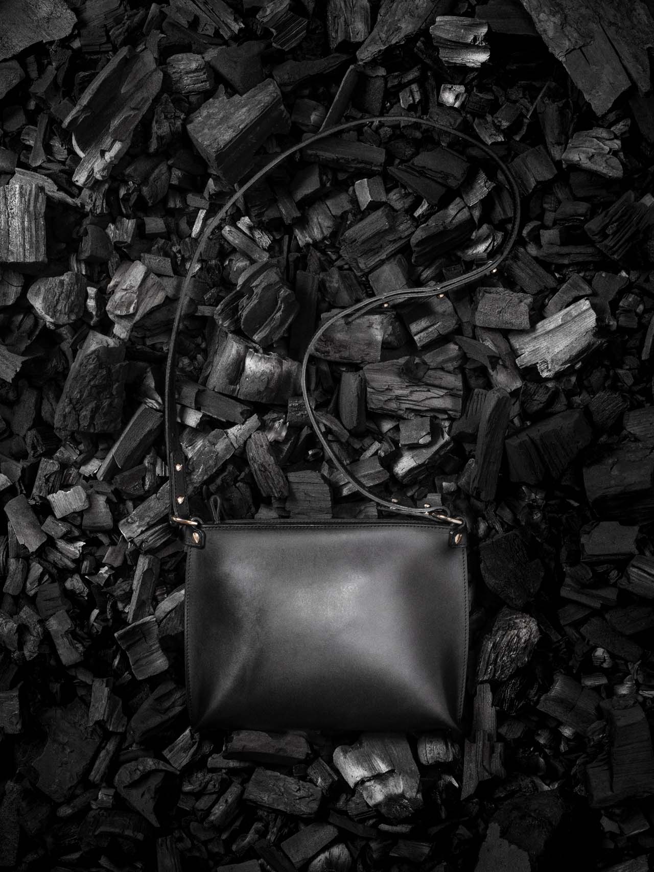 Sac à main en cuir noir Stella Soomlais à tannage végétal posé à plat sur un lit de charbon