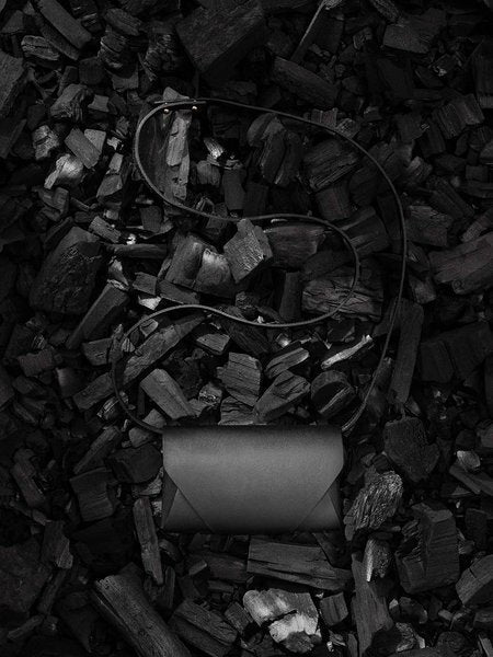 Pochette-portefeuille en cuir noir Stella Soomlais au tannage végétal posée sur du charbon de bois