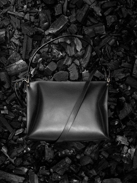 Sac à main en cuir noir Nothing to Declare Stella Soomlais, posé sur un lit de charbon de bois