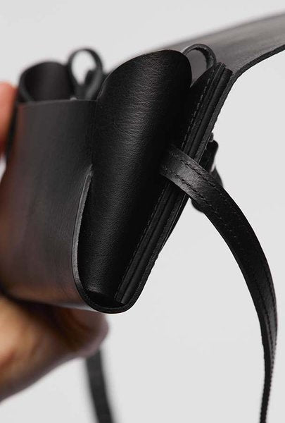Gros plan sur l'intérieur ouvert de la pochette-portefeuille en cuir noir Stella Soomlais et sa lanière réglable