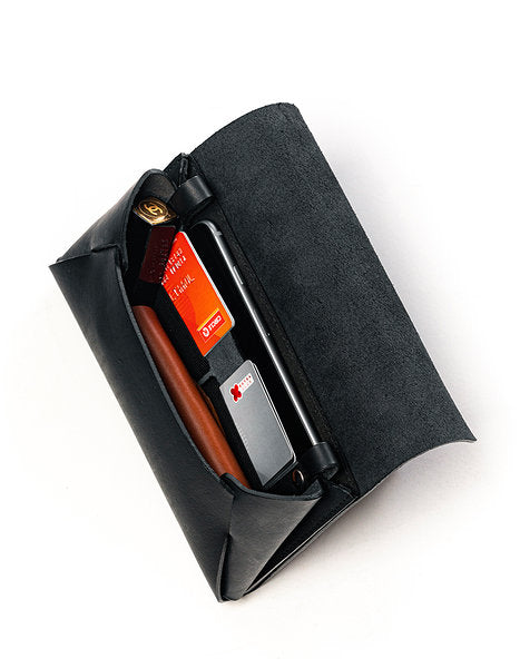 Pochette-portefeuille en cuir noir Stella Soomlais ouverte, téléphone, cartes et stylo rangés dans les compartiments