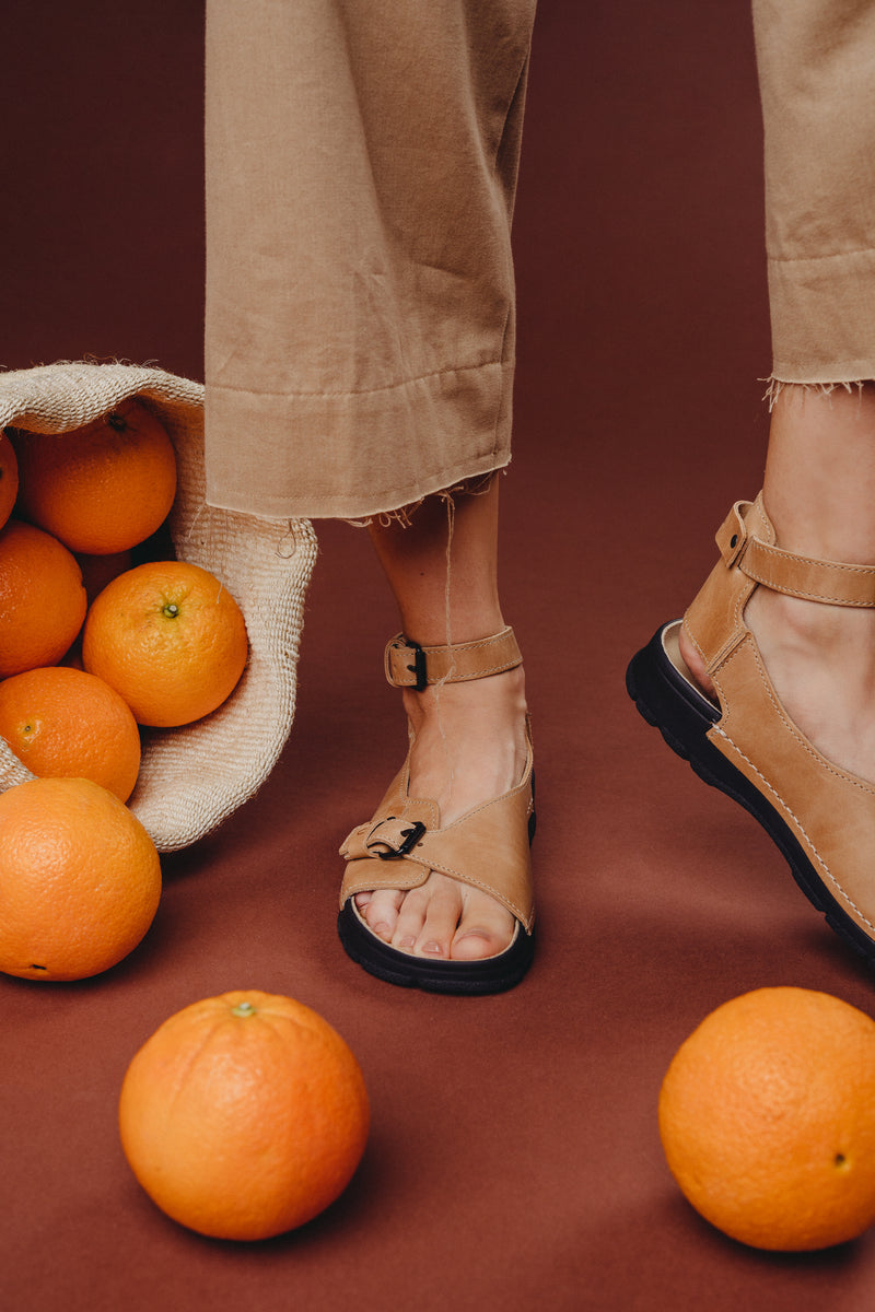 Sandales en cuir beige à sangle réglable, panier d'oranges sur fond brun