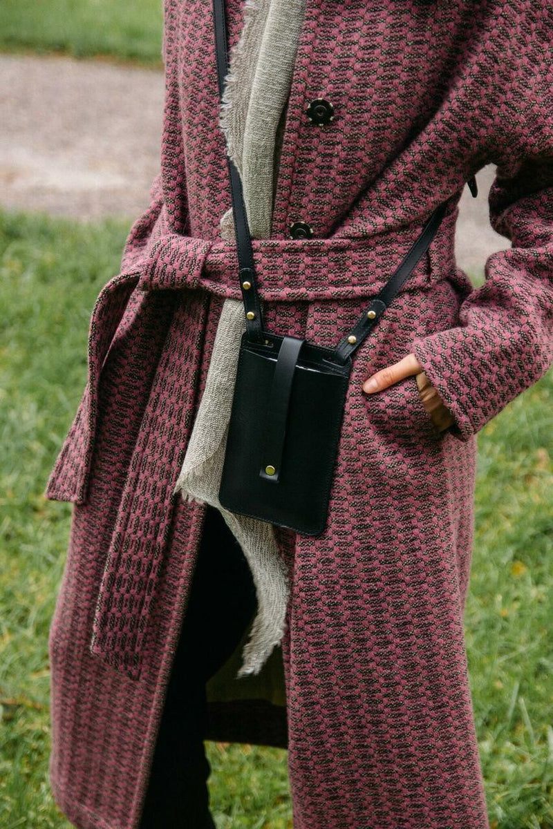 Pochette téléphone en cuir noir Stella Soomlais portée en bandoulière sur un manteau en tweed rose
