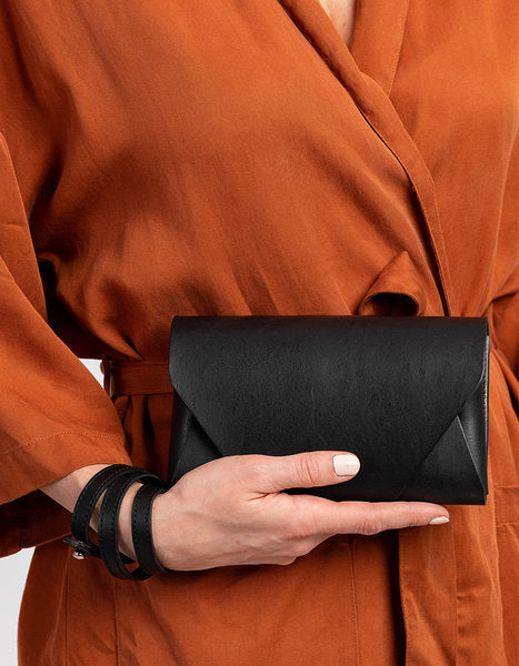 Pochette-portefeuille en cuir noir Stella Soomlais tenue à une main devant la taille, vue de face du rabat