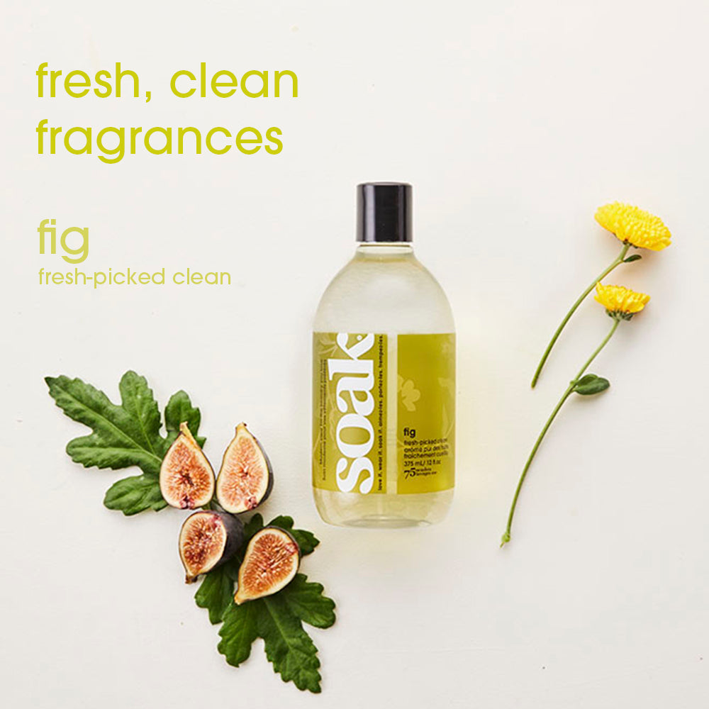 Flacon de lessive Soak Fig 375 ml entouré de figues fraîches et de fleurs jaunes, mise à plat