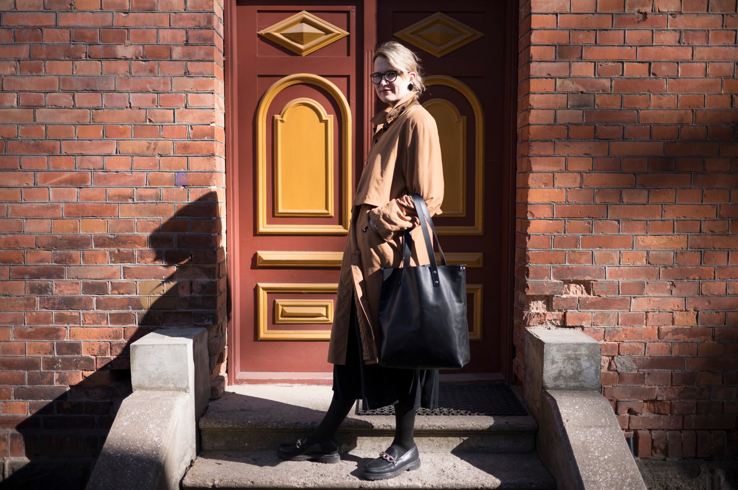 Sac cabas en cuir noir Stella Soomlais, porté au bras devant une porte ancienne